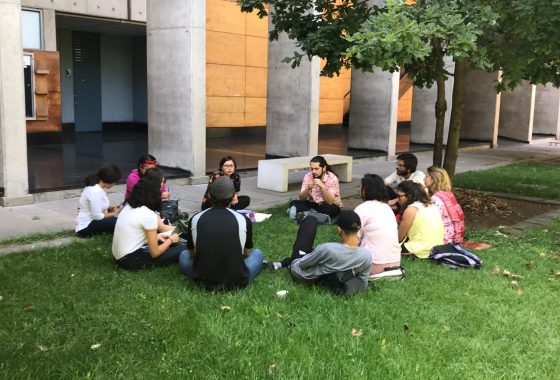 La imagen muestra a un grupo de estudiantes junto a la Tutora Rosio Rivera sentados en el pasto del patio de Humanidades del Campus San Joaquín de la UC. El grupo de discusión forma parte del Cabildo desarrollado por el programa en el mes de octubre de 2019.