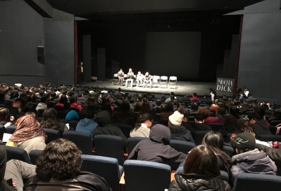La imagen muestra el escenario del Teatro UC con cuatro actores que forman parte del elenco de la obra Mocha Dick. El teatro se encuentra lleno de estudiantes de liceos PACE UC que participan del conversatorio realizado por el elenco de la obra en mayo de 2019.