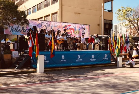 La imagen muestra el escenario de la celebración del Día de la Interculturalidad organizado en el Liceo Presidente Gabriel González Videla A24 como parte de los Proyectos Participativos ejecutados en 2019. En el escenario se presenta el taller de música del liceo, compuesto por estudiantes de distintos niveles y su profesora Valentina Roca.
