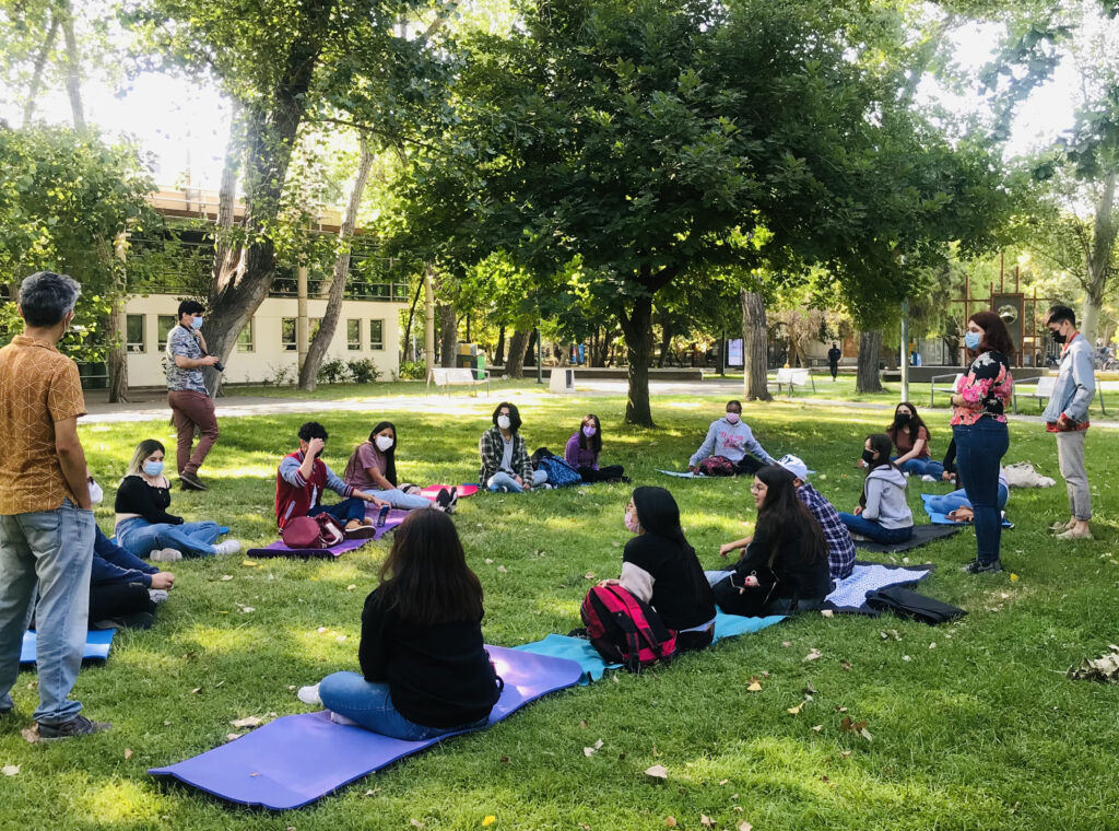 Estudiantes de PACE UC sentados en circulos en pastos del Campus San Joaquín UC en actividad presencial, con mascarillas.