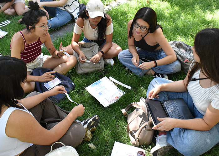 Foto tomada desde arriba, de un grupo de estudiantes sentadas en círculo, con papeles y computadores.