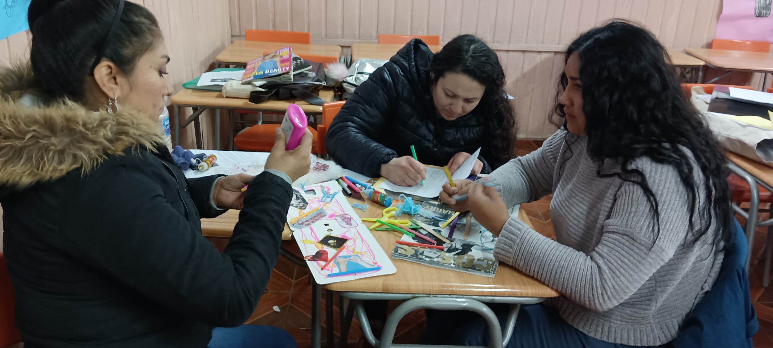 Grupo pequeño de mujeres sentadas en una sala de clases con materiales en sus manos
