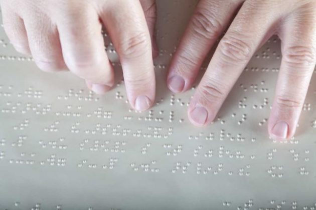 Manos estudiante ciega leyendo libro en Braille.