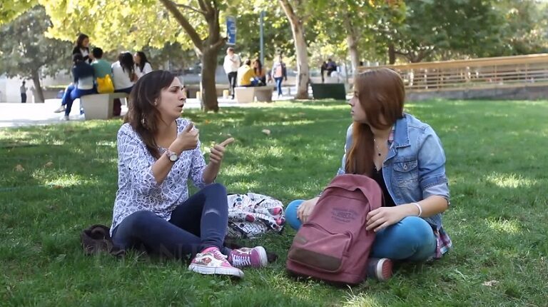 Estudiantes comunicándose en Lengua de Señas Chilena sentadas en pastos del Campus San Joaquín UC.