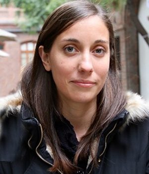Foto facial de profesional de PACE UC, Beatriz Santelices, en fondo de edificio café.