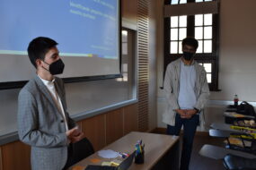 Profesional de la Dirección de Inclusión junto a estudiante de Antropología UC hablando en capacitación indicando elementos de una presentación PPT proyectada en un telón