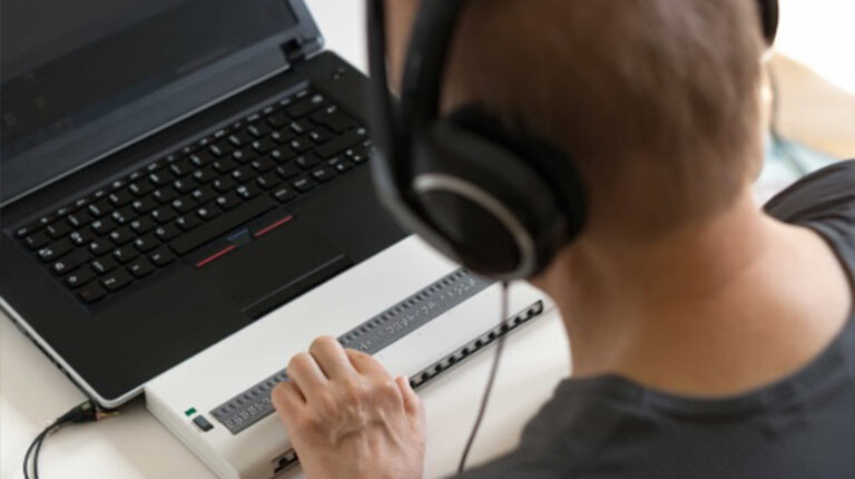 Foto de una persona por detrás, utilizando audífonos grandes frente a un computador, usando un teclado adaptado.