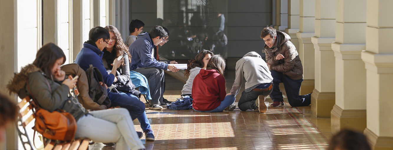 Estudiantes en un pasillo conversando, sentados en bancas y en el suelo.