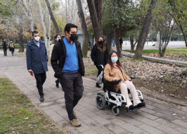 Fotografía de personas adultas con mascarilla caminando, una de ellas es usuaria de silla de ruedas.