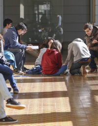 Fotografía de estudiantes sentados en el suelo conversando.