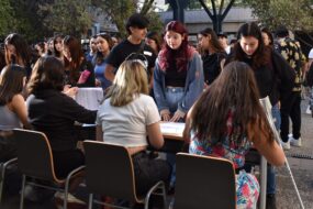 Foto de estudiantes UC realizando filas frente a una mesa con personas con listas en sus manos