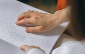 Fotografía de las manos de dos personas sobre un libro en lenguaje Braille