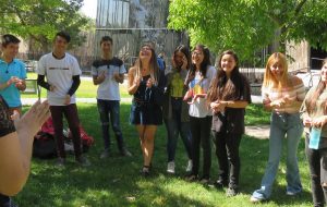 Alumnos y alumnas de PACE UC sonriendo y aplaudiendo en actividad dirigida por tutora del programa, realizada en el patio exterior del edificio Cddoc en Campus San Joaquín.
