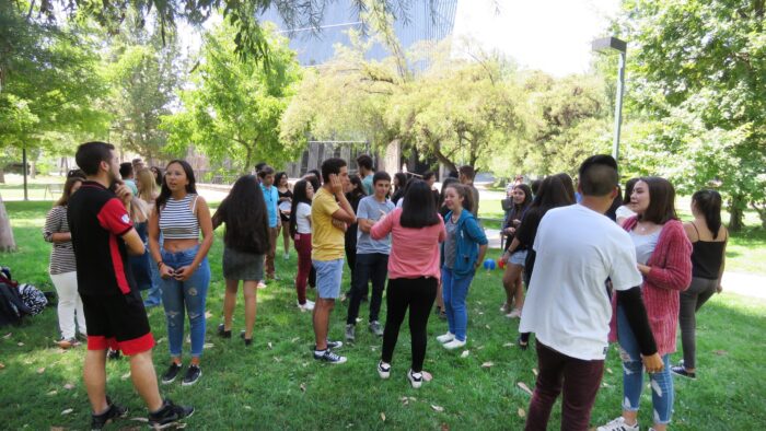 Estudiantes que ingresaron en 2019 por la vía Cupo PACE UC en explanada de Campus San Joaquín frente al Edificio Cddoc de pie realizando una actividad recreacional en grupos de dos y tres personas.
