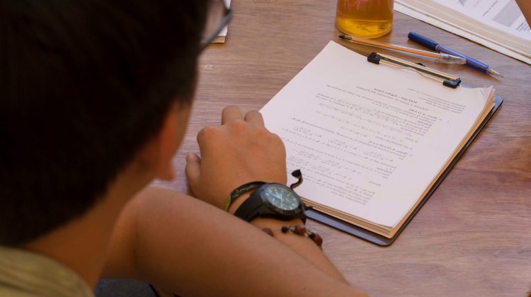 Estudiante con sus manos sobre una mesa y un cuadernillo.