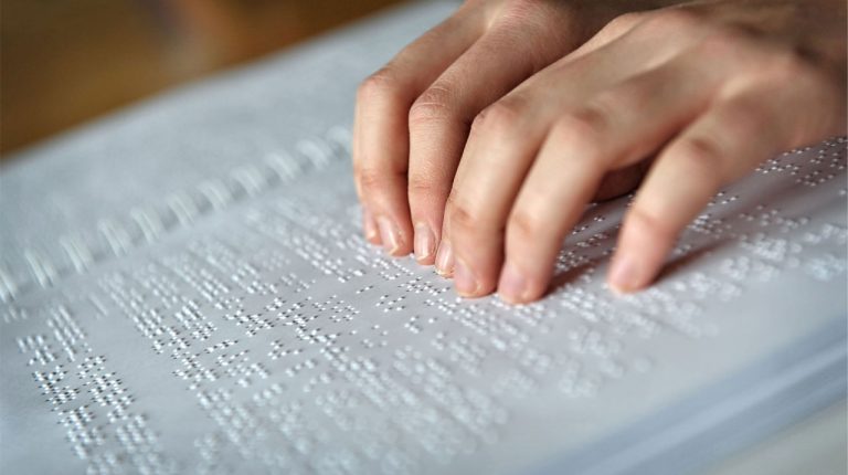 Manos sobre cuaderno con escritura en Braille.