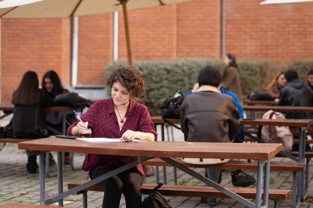 Estudiante sentada al aire libre en una mesa de madera, escribiendo en papel