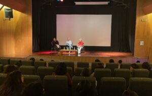 Escenario de Cine UC e imagen de 3 panelistas que participan de conversatorio