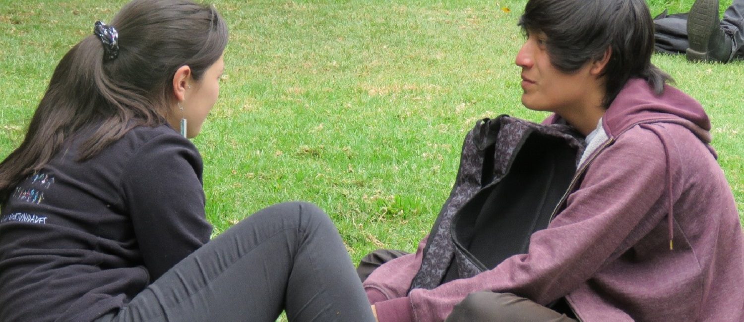 Tutora de PACE UC en sesión de apoyo con estudiante del programa, sentados en explanada de pasto en Campus San Joaquín.