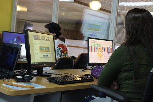 Alumna usuaria de silla de ruedas, aparece de espalda trabajando en computadores de sala Crisol.